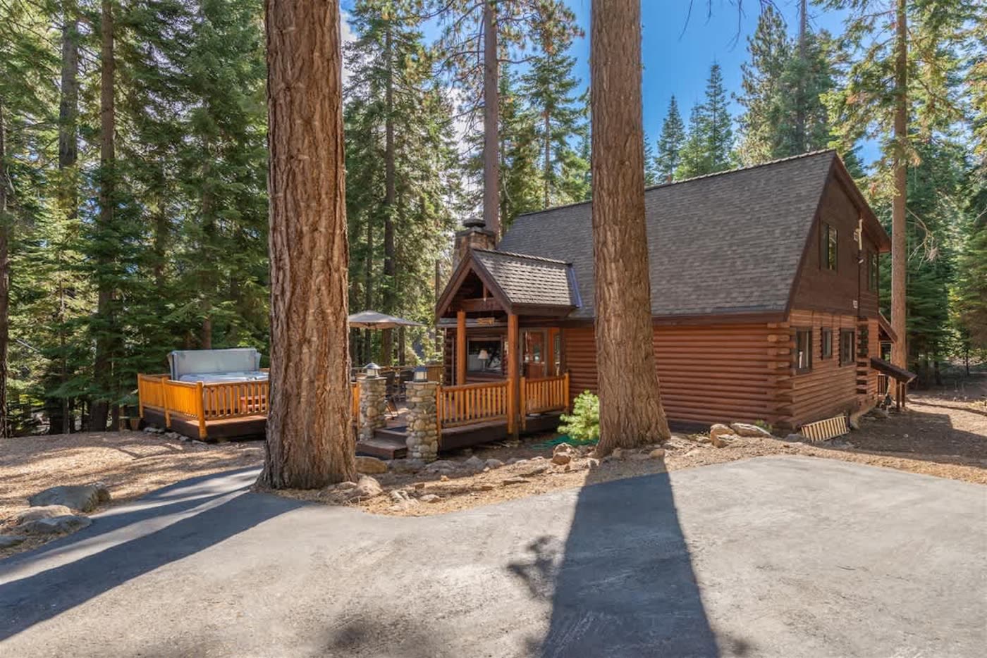 The front of Tahoe Bound before: a gravel drive and bare ground between the pines, cabin unlit